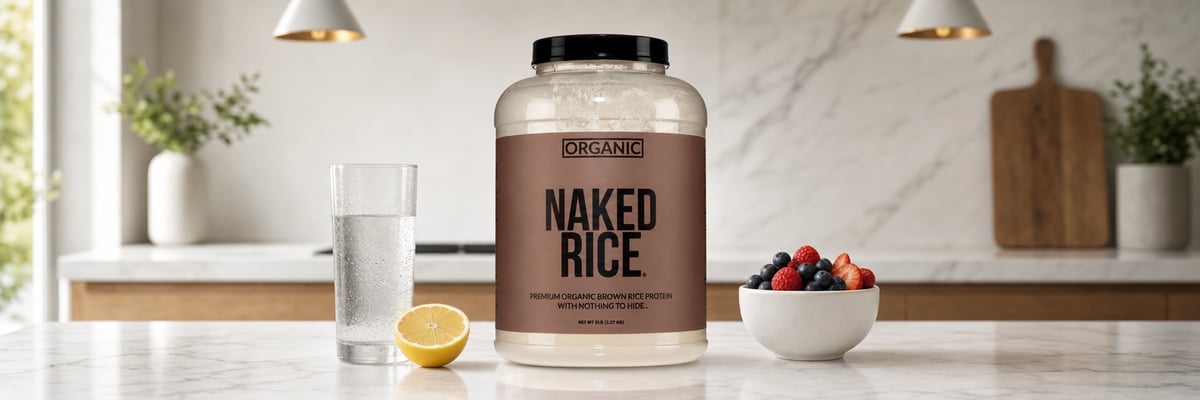 Naked Rice protein tub on marble kitchen counter with berries, lemon, and water glass